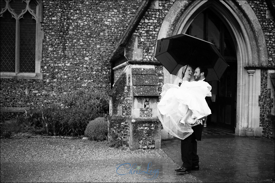 Bride being carried by groom as they leave the church in the rain